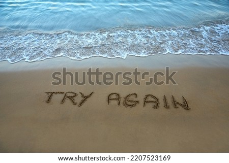 Try again written in the sand on the beach with the sea washing up the shore