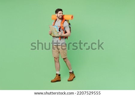 Full body mountaineer young traveler white man carry backpack stuff mat walk read map look aside isolated on plain green background. Tourist leads active lifestyle Hiking trek rest travel trip concept