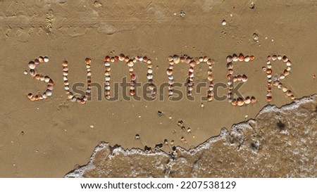 Summer inscription on the sand. The word summer laid out with shells on the sand and a sea wave. Letters made by Shells. Stock Photo.