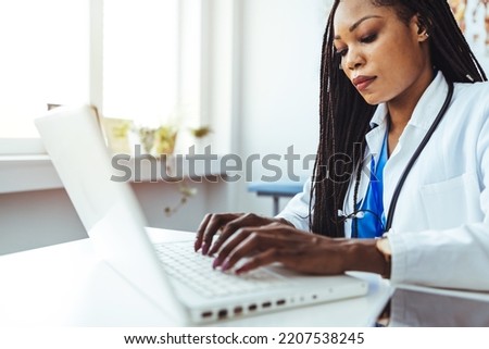 Woman watching a laptop screen while stretching her hand and typing on it. Doctor clicking on a laptop.  Female doctor using laptop with mockup on screen for medical work at modern hospital office