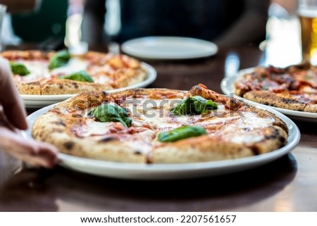 Close up view of a Margherita Neapolitan style pizza with buffalo mozzarella, tomato sauce and basil - Waiter hand serving pizza at pizza restaurant Royalty-Free Stock Photo #2207561657