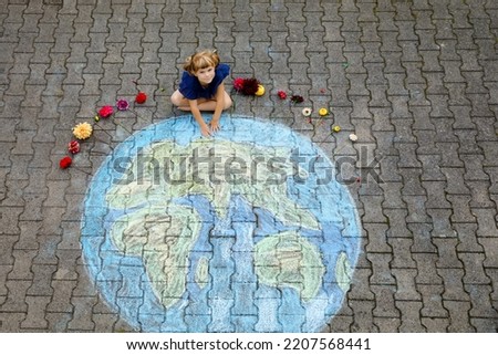 Little preschool girl with flowers and earth globe painting with colorful chalks on ground. Positive toddler child. Happy earth day concept. Creation of children for saving world, environment ecology
