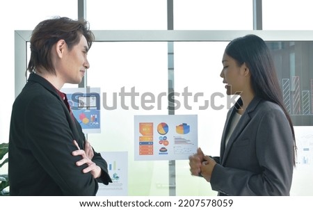 Asian business man and woman looking at paper note stick on glass board to discuss and working in office  