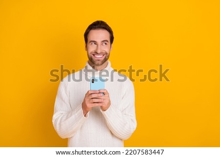 Photo of cheerful dreamy guy dressed white sweater writing modern device empty space isolated yellow color background