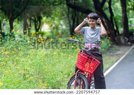 Asian women exercise in the morning, ride a bike, wear headphones, listen to music, enjoy in the park. Healthy fitness concept