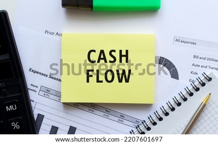 Text CASH FLOW on the page of a notepad lying on financial charts on the office desk.