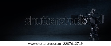 Digital movie camera in the dark. Video camera on a tripod in a black contre room with light and shadow. Tv documentary or movie production banner background with copy space Royalty-Free Stock Photo #2207613719