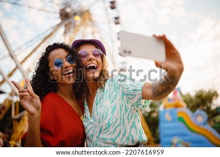Young multiracial women taking selfie on cellphone while spending time in attraction park