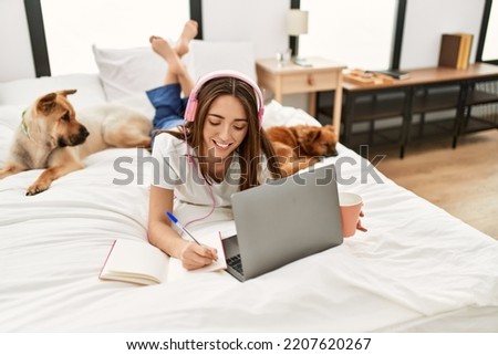 Young hispanic woman studying lying on bed with dogs at bedroom