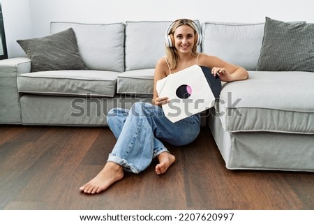 Young blonde woman listening to music holding vinyl disc at home