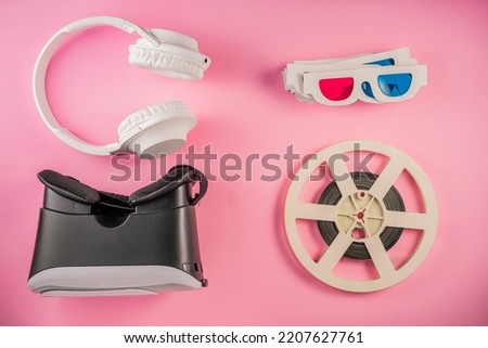 Old paper 3D glasses with red-blue lenses, black virtual reality headset. White headphones and a plastic retro tape reel on a pink background. Retro background with antiques, nostalgia.