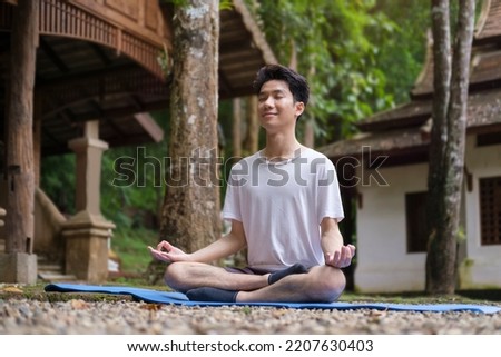 Peaceful man meditating sitting in lotus pose on green grass. Yoga, pilates, fitness, healthy lifestyle concept.
