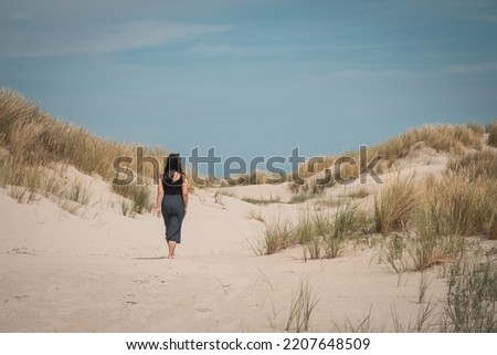 Young girl (woman) going for a walk in the dunes and sand beach on the Northsea coast of the german island Juist. Blue clouded sky and bushes of grass. Perfect summer trip.