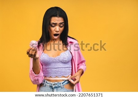 American african girl worried does not eat cake. Conception to lose weight. Hand gesturing no to a cake. Isolated over yellow background. Using measure tape.
