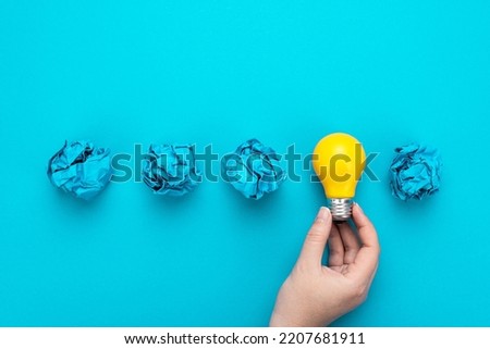 One person have great idea during brainstorming session concept. Great idea concept with bulb in hand and crumpled office paper. Conceptual photo of light bulb in human hand over turquoise background. Royalty-Free Stock Photo #2207681911