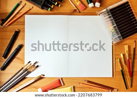 Creative artist mockup workplace on wooden table . Flat lay, top view with blank sketchbook with copyspace, pencils, paintbrushes and paints. Art, workshop, painting, drawing, craft, creativity.