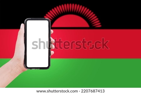 Close-up of male hand holding smartphone with blank on screen, on background of blurred flag of Malawi.