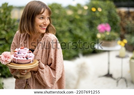 Young cheerful woman stands with festive cheesecake in garden. Happy holiday and celebration concept