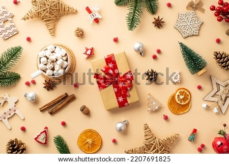Top view photo of christmas decorations giftbox baubles wicker stars wood ornaments jingle bell acorns pine branches cones mug of cocoa mistletoe and dried citrus slices on isolated beige background