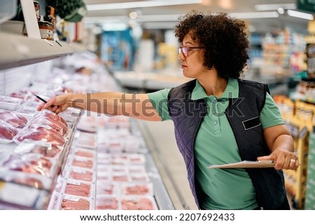Super market manager checking frozen products in refrigerated section.  Royalty-Free Stock Photo #2207692433
