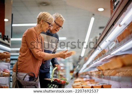 Senior woman and her husband choosing food at refrigerated section while shopping in supermarket. Royalty-Free Stock Photo #2207692537