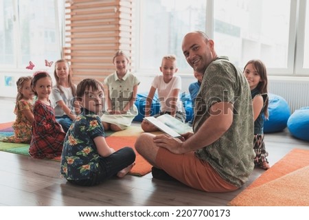Reading time in elementary school or kindergarten, teacher reading a book to kids in elementary school or kindergaden. Selective focus  Royalty-Free Stock Photo #2207700173