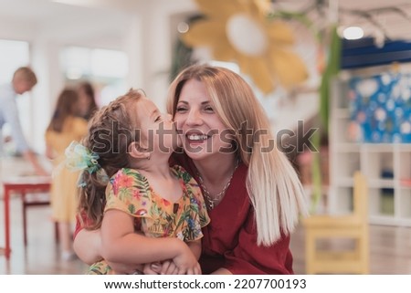 A cute little girl kisses and hugs her mother in preschool
