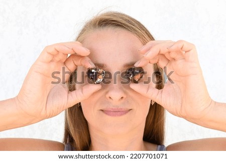 Young blonde woman holds two chocolate hearts in her hands and uses them instead of eyes. Close up portrait.