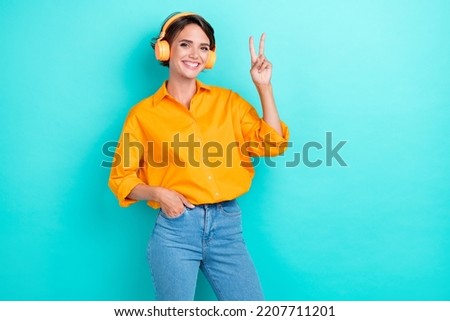 Portrait photo of young adorable woman wear shirt listening music wireless headphones technology showing v-sign symbol positive advert isolated on cyan color background