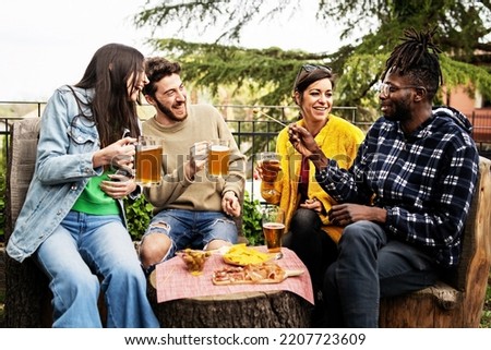 Happy multiethnic friends talking, clinking and toasting beer at brewery bar restaurant patio - Life style and beverage concept with young people having fun together out side