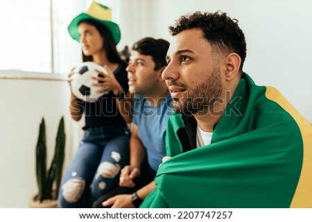Nervous and excited sports fans watching game on TV at home. Nervous friends watching football game on the sofa. Royalty-Free Stock Photo #2207747257