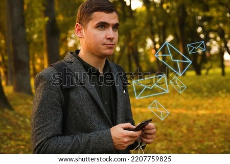 Defocus young man holding phone. Man using smart phone in autumn park. Typing text message or reading social media at mobile phone. Fall. Cell phone. Backpack. Digital business. Out of focus.