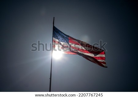 The United States of the American flag blowing in the wind of a bright sunny day with the sun behind it