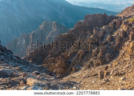 Vastness sunny mountain view from cliff at very high altitude. Scenic alpine landscape with beautiful sharp rocks and couloirs in sunlight. Beautiful mountain scenery on abyss edge with sharp stones. Royalty-Free Stock Photo #2207778885