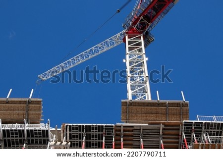 A construction crane is seen on a clear sky day, while on-site building a condo, apartment building.  