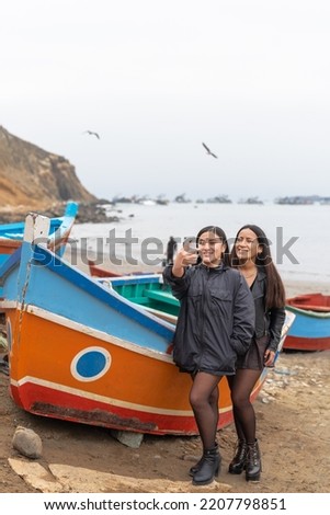 Vertical photo of latin friends taking a selfie on a beach full of colorful boats