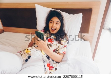 Happy young woman checking on her phone while lying in bed