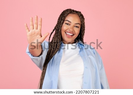 Hello. Happy Black Plus Size Woman Waving Hand Smiling To Camera Posing Standing In Studio On Pink Background. Hi Greeting Gesture, Advertisement Banner Concept Royalty-Free Stock Photo #2207807221