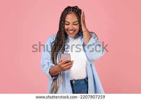 Excited African American Woman Using Cellphone Reading Positive Message Texting Standing In Studio Over Pink Background. Obese Lady Using New Application. Wow Mobile App Concept