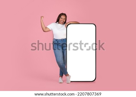 Cheerful Black Oversized Woman Posing Near Huge Smartphone With Blank Screen Posing Gesturing Yes Over Pink Studio Background. Mobile App Ad. Mockup, Full Length Shot