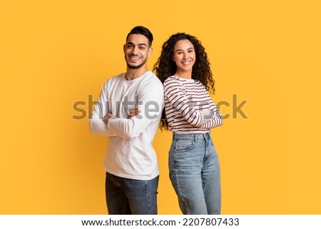 Portrait Of Cheerful Young Middle Eastern Man And Woman Posing Over Yellow Background, Happy Millennial Arab Male And Female Standing With Folded Arms And Smiling At Camera, Copy Space