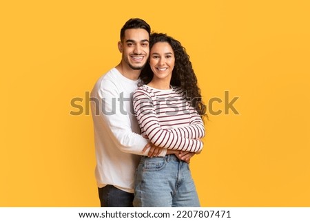 Portrait Of Loving Young Arab Man And Woman Embracing And Smiling At Camera, Romantic Middle Eastern Couple Hugging While Posing Together Over Yellow Background In Studio, Copy Space Royalty-Free Stock Photo #2207807471