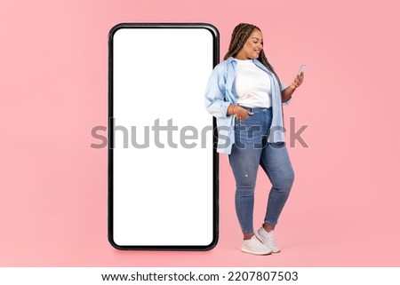 African American Oversized Lady Leaning On Big Phone With Empty Screen Texting And Using Application On Smartphone Standing Over Pink Studio Background. Mobile Communication. Mockup Royalty-Free Stock Photo #2207807503