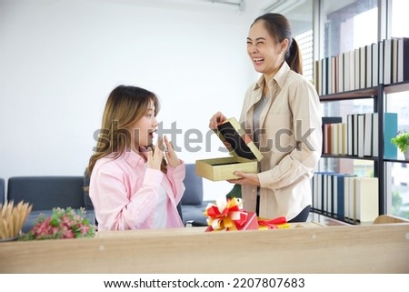 boss or manager giving and showing inside gift box to young woman on a table in the office