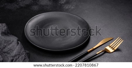 An empty black plate on a dark concrete background with spices, herbs and cutlery. Home dinner cooking Royalty-Free Stock Photo #2207810867