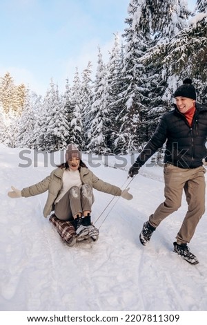 Young couple in love is sledding in a winter forest and having fun spending time together.Winter,active lifestyle,Valentine's day,newlyweds,tenderness and love.