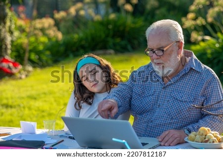 Grandfather explains how to use laptop to his granddaughter