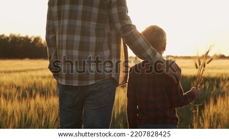 Farmer and his son in front of a sunset agricultural landscape. Man and a boy in a countryside field. Fatherhood, country life, farming and country lifestyle. Royalty-Free Stock Photo #2207828425