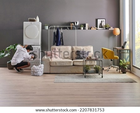 Young man is living at minimalist home style, working laptop, laundry, washing machine, looking phone at the room, grey wall background and decorative interior. Royalty-Free Stock Photo #2207831753