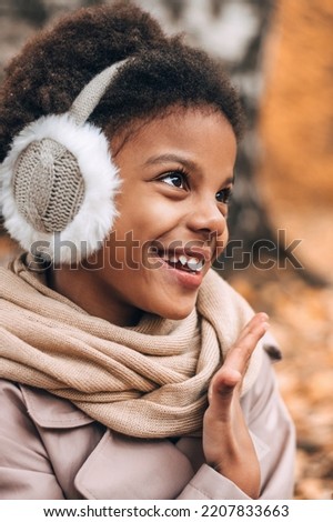 Portrait of a cute happy African-American girl in fur headphones in an autumn park.Diversity,autumn concept.
